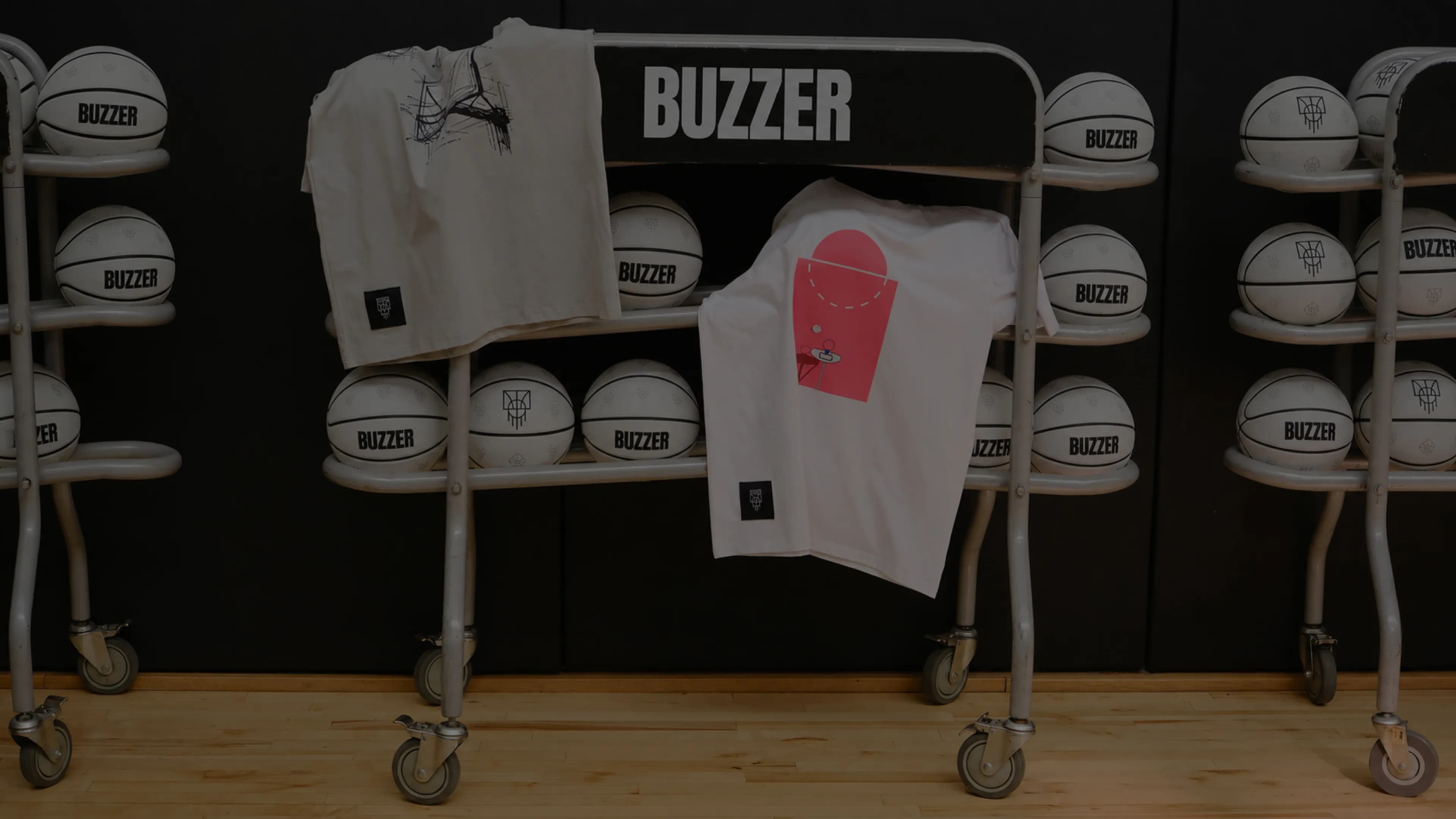 Стойки с мячами BUZZER и футболками бренда в зале с паркетным полом.